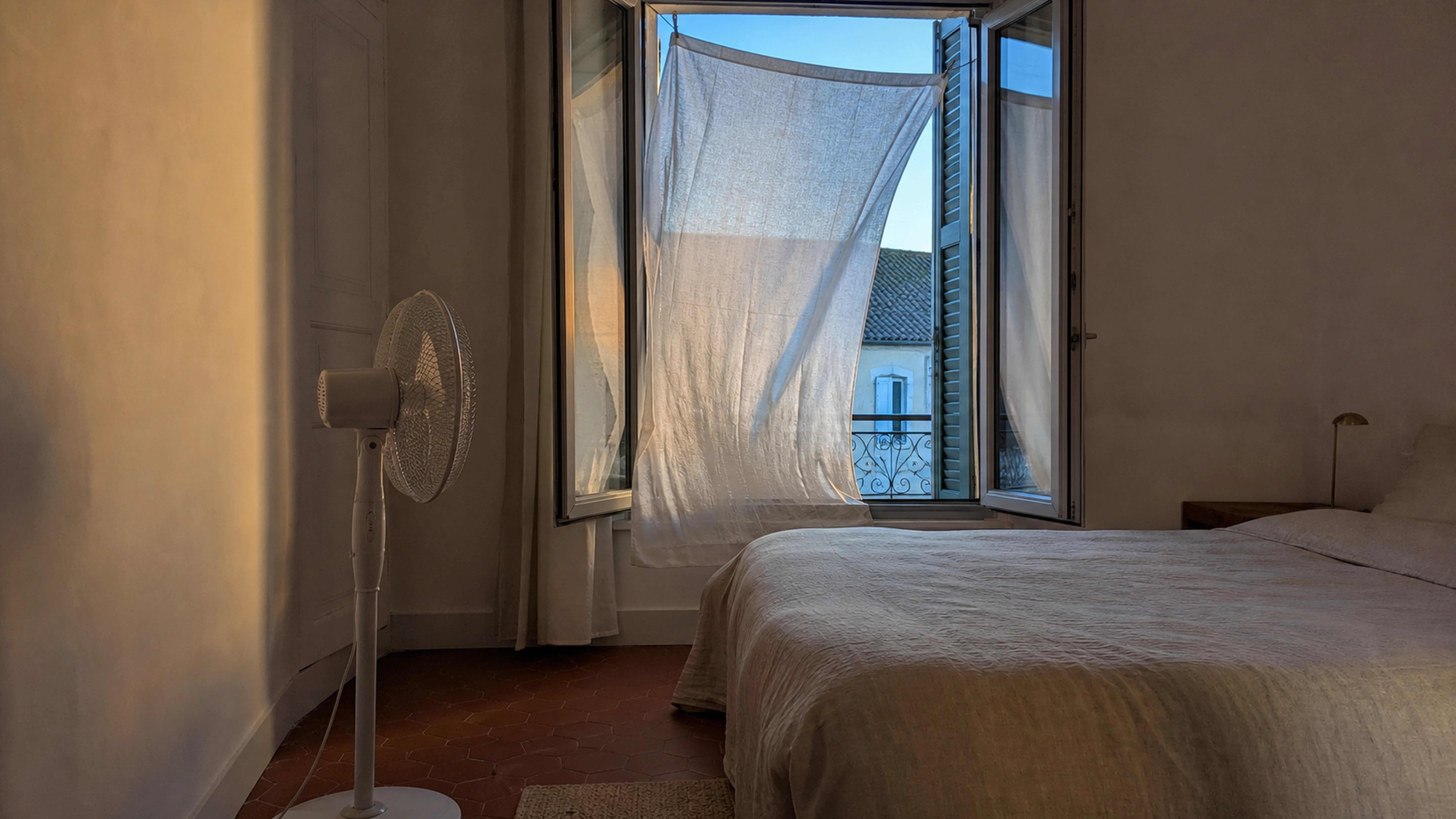 Chambre aérée au crépuscule avec un drap léger devant la fenêtre et un ventilateur