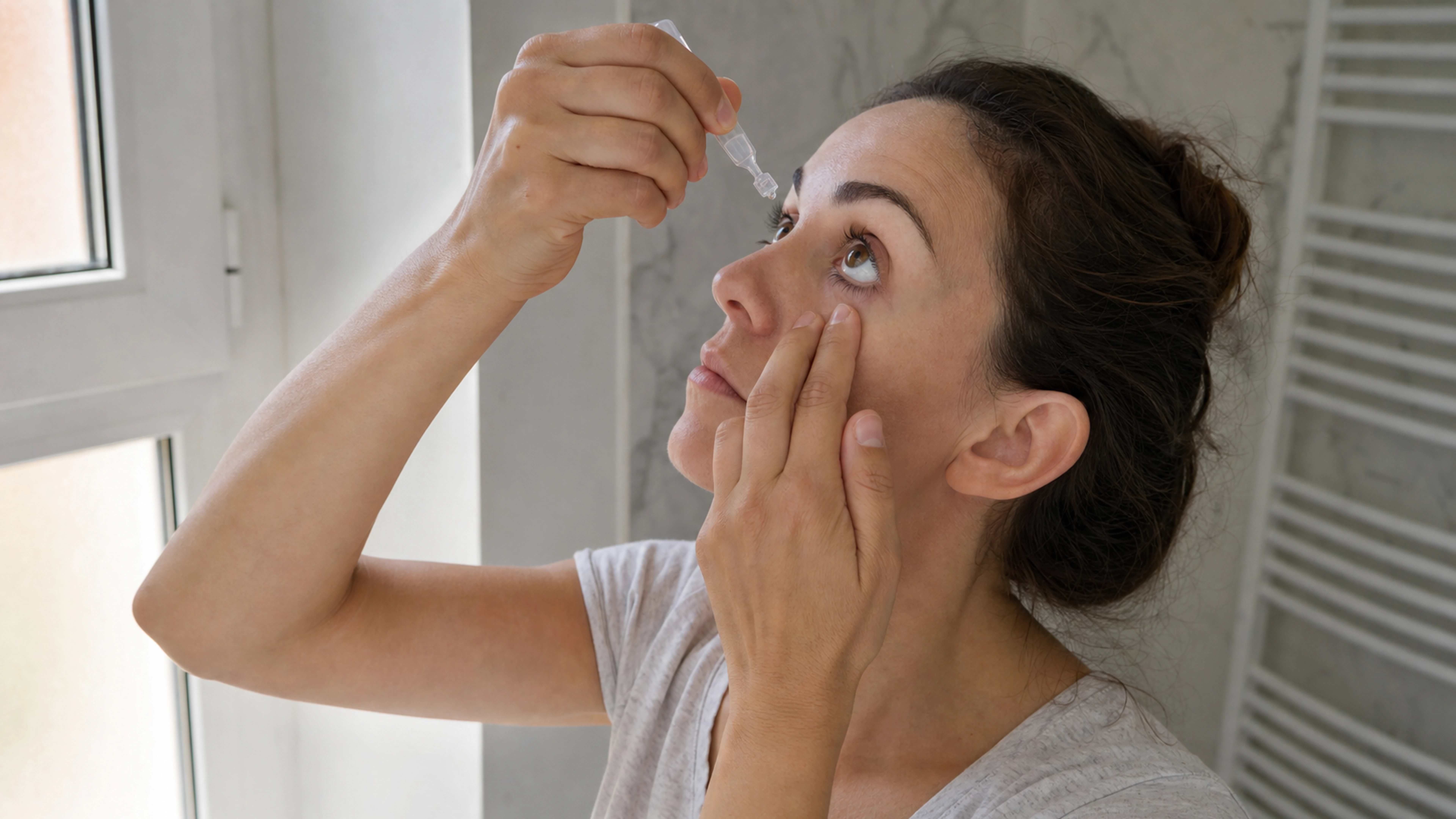 Personne appliquant une goutte ophtalmique avec une unidose près d’une fenêtre
